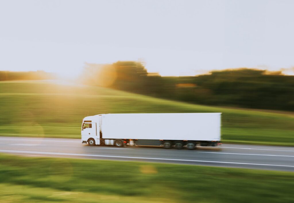 A fast-moving white cargo truck drives through the countryside on a sunny day in Belarus.