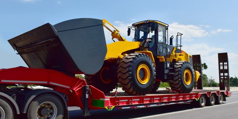 Big tractor machine heavy tool on truck transportation motion speed on road under blue sky